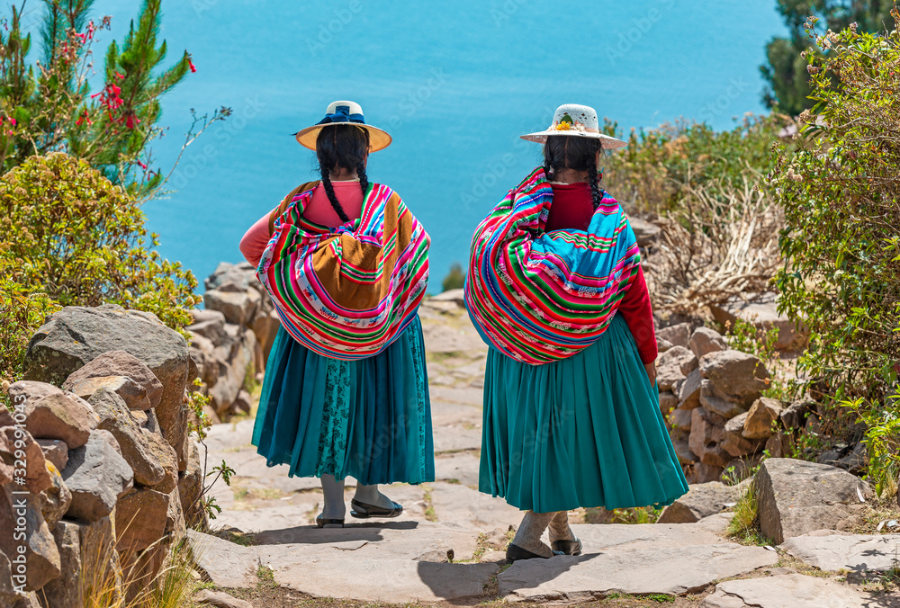 two-indigenous-quechua-women-in-traditional-clothes-walking-down-the-path-to-the-harbor-of-isla-taquile-taquile-island-with-the-titicaca-lake-in-the-background-peru-stockpack-adobe-stock Two indigenous Quechua women in traditional clothes walking down the path to the harbor of Isla Taquile (Taquile Island) with the Titicaca Lake in the background, Peru.